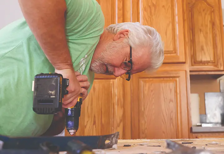 An older man drilling a countertop